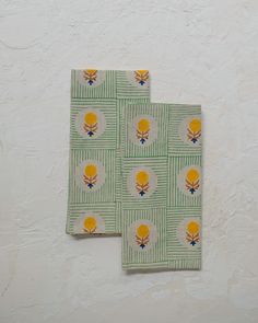 two napkins with yellow flowers on them sitting next to each other in front of a white wall