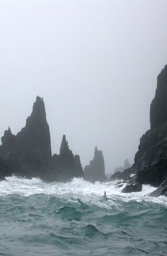 black and white photo of waves crashing on rocks in the ocean with foggy sky