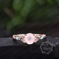 a pink ring with green and white stones on it's side, sitting on top of a black rock