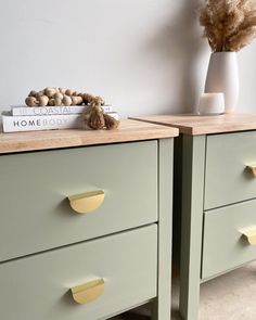 two green dressers with yellow handles and knobs on each side, next to a white vase filled with dried flowers