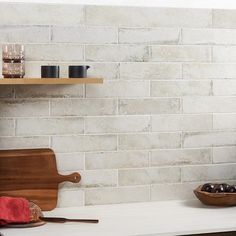 a white brick wall in a kitchen with wooden cutting board and bowl of cherries