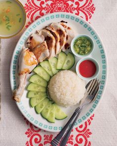 a plate with rice, cucumber and chicken on it next to sauces