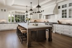 a large kitchen with white cabinets and wood flooring on the walls, along with an island that has stools in front of it