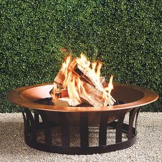 a fire pit sitting on top of a gravel ground next to a green hedge wall