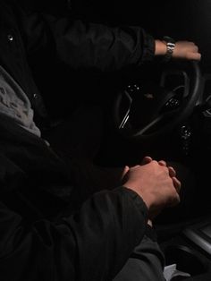 a man is driving in the dark with his hands on the steering wheel while wearing a black jacket