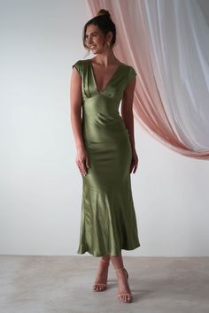 a woman standing in front of a curtain wearing a green dress and smiling at the camera