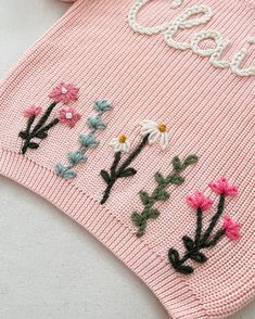 a pink sweater with embroidered flowers on the front and bottom, along with two pairs of scissors