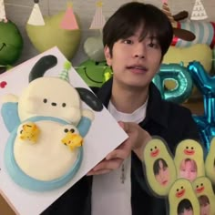 a young man holding up a cake in front of some balloons