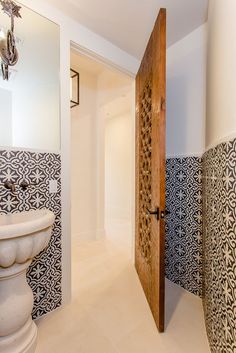 an open door leading to a bathroom with black and white tiles on the walls, along with a pedestal sink