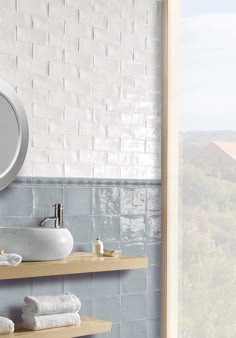 a bathroom with blue tile and wooden shelves under a round mirror on the wall next to two sinks