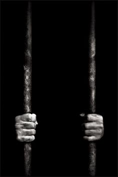 black and white photograph of two hands holding bars in front of a dark background with only one hand on the bars