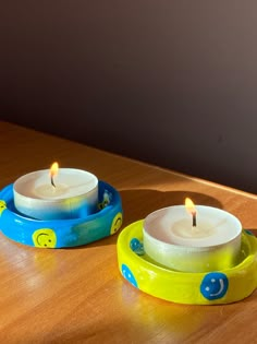 two lit candles sitting on top of a wooden table next to each other with smiley faces painted on them