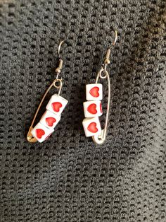 two red and white hearts are hanging from the earwires of some kind of earrings