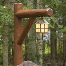 a lamp hanging from the side of a wooden pole next to a rock and trees