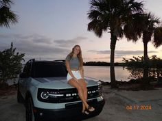 a woman is sitting on the hood of a truck near some palm trees and water