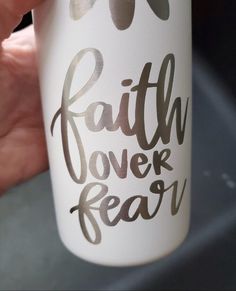 a hand holding a white coffee cup with the words faith over fear on it