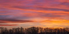 the sky is pink and orange as the sun sets over some trees in the distance