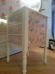 a white table with drawers on top of it and a pink wallpapered background