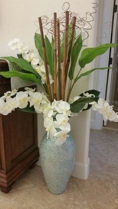 a blue vase with white flowers in it on the floor next to a wooden cabinet