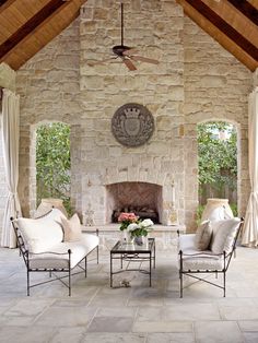 an outdoor living room with stone fireplace and chairs