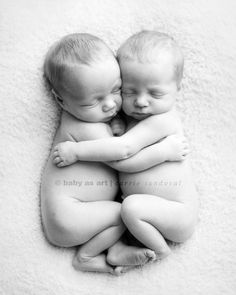 two baby babies cuddle together in the middle of a white blanket, with their heads touching each other