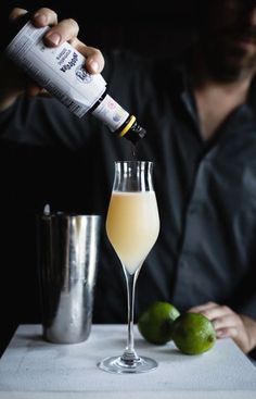 a man pouring an alcoholic drink into a glass next to limes and a shaker