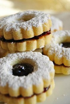 small pastries with jelly and powdered sugar are on a white plate, ready to be eaten