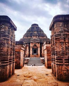 the entrance to an ancient temple with stone pillars and steps leading up to it, under a cloudy sky