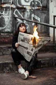 a woman sitting on the steps while holding a newspaper with flames coming out of it