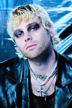 a man with blonde hair and blue eyes wearing a black leather jacket is looking at the camera