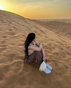 a woman is sitting in the sand with her hand on her knee and looking at the sky