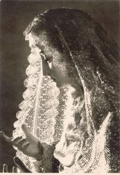 an old black and white photo of a woman wearing a shawl looking at her cell phone