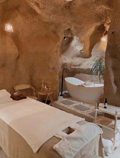 a room with a bed, bathtub and chair in it next to a stone wall