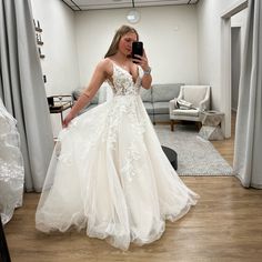 a woman in a wedding dress taking a selfie with her cell phone while standing in front of a couch