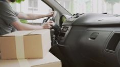 a man driving a truck with boxes on the back of it's seat and an open box in front of him