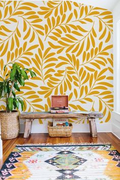 a room with a rug, potted plant and wooden bench in front of the wall