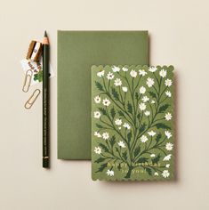 a green notebook with white daisies on it next to a pencil