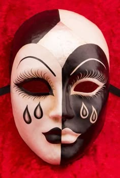 a black and white mask with tears on it's face sitting on a red surface