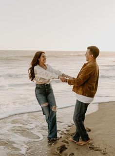 a man and woman holding hands on the beach with waves crashing in front of them