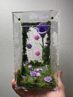 a person holding up a glass vase with flowers in it and moss on the inside