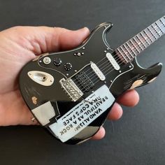 a person holding a miniature guitar shaped like a rock and roll record player's head