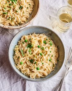 two bowls filled with pasta and peas on top of a table next to silverware