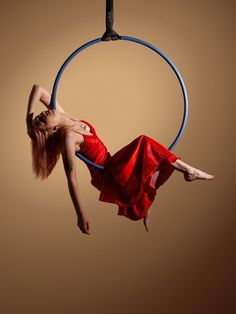 a woman in a red dress is doing aerial tricks on a hoop with one leg