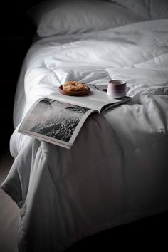 an open magazine sitting on top of a bed next to a cup and saucer