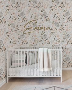 a white crib in front of a floral wallpaper