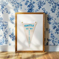 the seattle pennant is displayed in front of a blue floral wallpaper with a gold frame