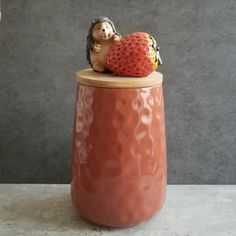 a ceramic hedge sitting on top of a strawberry in a vase with a wooden lid