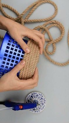 two hands holding a piece of jute rope over a blue and white container with holes in it