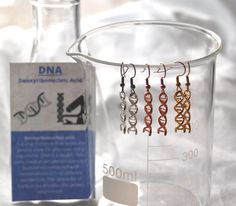 DNA MOLECULE EARRINGS * Material: Pendant (zinc alloy-based) on 316L Surgical Stainless Steel (Hypoallergenic) Earring Hooks (Fish Hook Style) with Rubber Earring Back *All material is lead and nickel free. *Earring Drop Length: 30 mm OTHER ∙ INFORMATION * All items are packaged ready to gift in white silk jewelry bags with an information card about the molecule (see video) - great as a gift! * If you can't find the information you need feel free to contact us. We are fast to reply :) TURN ∙ ARO Science Accessories Men, Chemical Earrings, Beaker Earrings, Science Earrings, Dna Molecule, Nerdy Gifts, Silk Jewelry, Free Earrings, Hypoallergenic Earrings