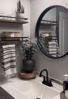 a bathroom sink sitting under a mirror next to a black and white potted plant